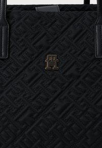 Czarna pikowana torba na ramię wykonana z teksturowanej tkaniny, z emblematem logo w złotym odcieniu i podwójnymi czarnymi skórzanymi uchwytami.