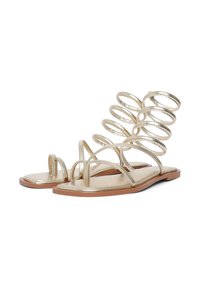 Metallic gold flat sandals featuring spiral strap design, open toe, and tan sole, with minimalistic construction and smooth texture.