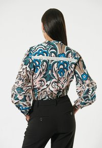 Bunte Bluse mit aufwendigen Blumendrucken in Türkis, Pink und Creme. Verfügt über voluminöse Ärmel und eine dekorative Lochspitze.