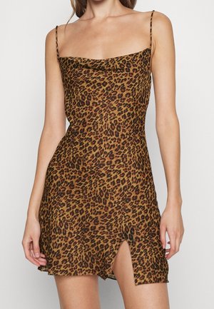 Femme portant une mini robe sans manches à imprimé léopard, avec des bretelles fines et une fente à l'avant cuisse.