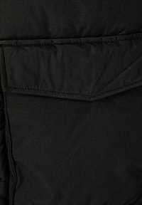 Črn puhafast jakna iz tkanine z gladko teksturo, opremljena z velikim, poševnim žepom in prešitimi trakovi za izolacijo in toploto.