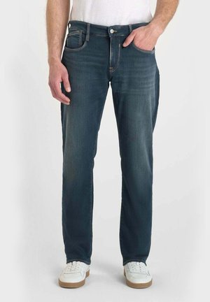 Dunkelblaue Denim-Jeans mit geradem Bein, im Five-Pocket-Stil und kontrastierendem gelben Stich, kombiniert mit weißen Sneakern.
