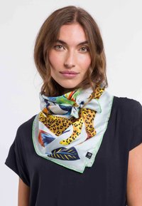 Foulard di seta con un motivo multicolore caratterizzato da macchie di leopardo e foglie tropicali, bordato da un accento verde. Indossato attorno al collo.