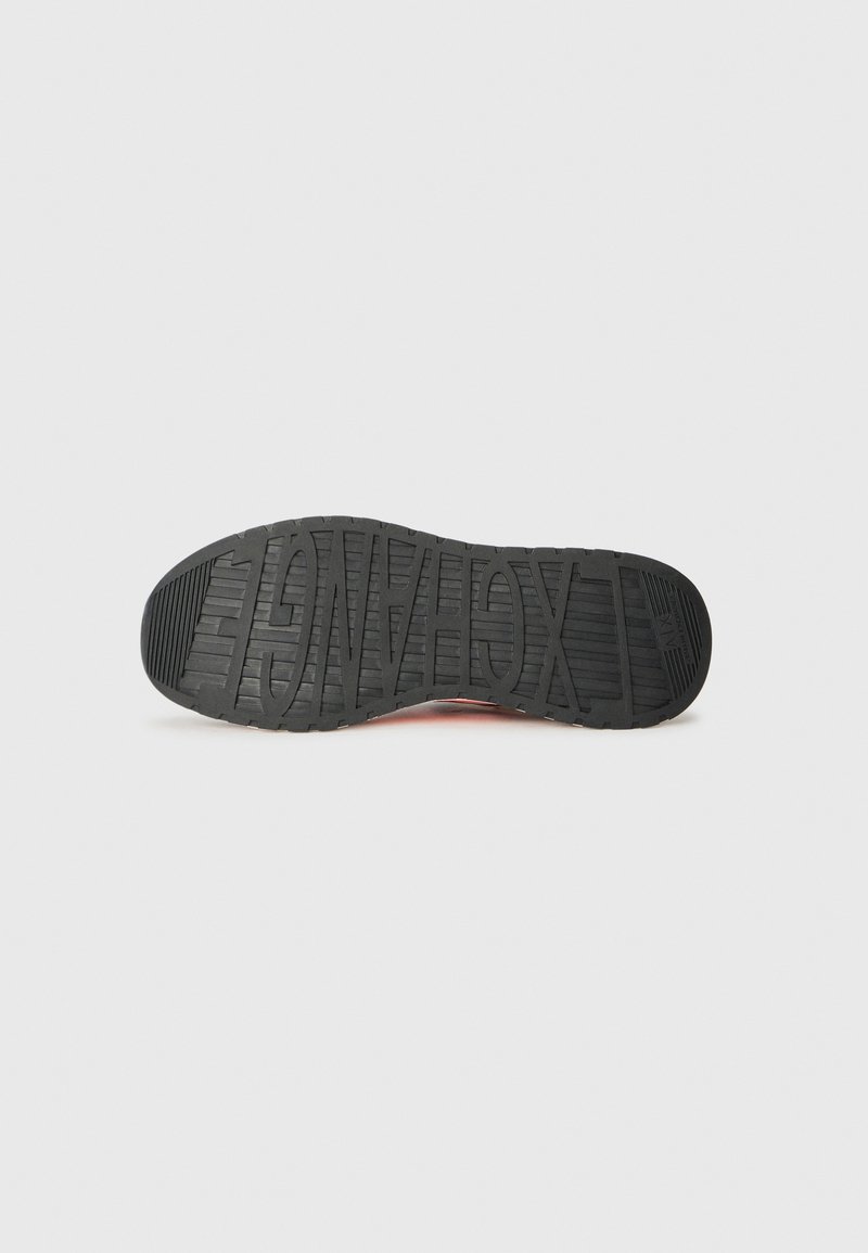 Suela de zapato de goma negra con superficie texturizada, que presenta patrones de agarre prominentes y logos en relieve. Bordes lisos, diseño de punta redondeada.