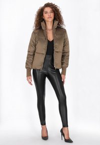 Puszysta oliwkowa kurtka typu bomber z wysokim kołnierzem, czarne dopasowane spodnie oraz czarne wąskie szpilki z srebrnymi ćwiekami.