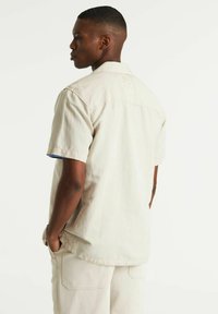 Korte mouwen, lichtbeige shirt gemaakt van zachte stof met een relaxte pasvorm. Heeft een blauwe accent aan de binnenkant van de mouwen.