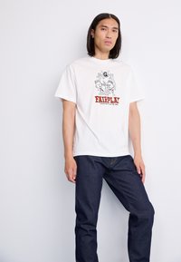Witte katoenen T-shirt met een zwarte grafische bedrukking en rode tekst "FAIRPLAY". Gecombineerd met donkerblauwe spijkerbroek. Casual pasvorm, korte mouwen.