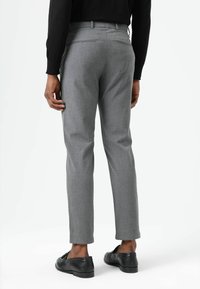 Lichtgrijze broek met een getailleerde pasvorm, voorzien van twee achterzakken en een gladde textuur, gecombineerd met zwarte loafers.