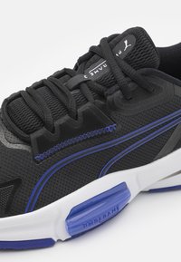 Zwarte sportieve schoen met een bovenwerk van mesh, paarse accenten, gestructureerde veters en een witte zool met blauwe demping en branding.