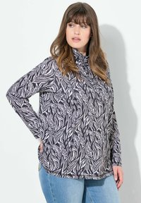 Top à manches longues noir et blanc avec un motif de feuilles, un col montant et des poches latérales, associé à un jean en denim bleu.