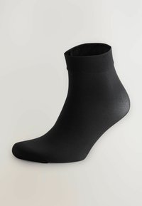 Svart ankelsocka med vikbar mudd, visad på en fotsformad hållare mot en enkel ljus bakgrund.