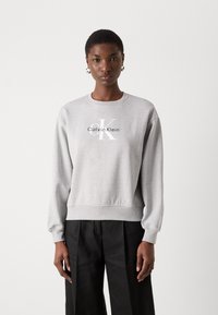 Gray cotton sweatshirt with a round neckline, ribbed cuffs, and hem. Features a white logo "Calvin Klein" and "CK" printed on the front.