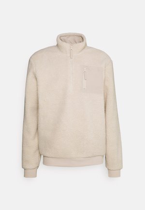 Beiger Fleece-Pullover mit hohem Kragen, halbseitigem Reißverschluss vorne und einer Brusttasche. Weicher Stoff mit gerippten Bündchen und Saumdetail.