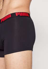 Bóxers negros con un logo rojo de Puma en la cinturilla. La tela es suave y ajustada, con un diseño sin costuras.