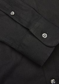 Czarna koszula z długimi rękawami, wykonana z teksturowanej tkaniny, z standardowym zapięciem na guziki i srebrnymi guzikami na mankietach. Charakteryzuje się minimalistycznym wzornictwem.