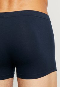 Boxeri din bumbac albastru marin, cu o textură moale și netedă, având un elastic fără cusături și un fit strâns. Detaliul subtil cu logo este vizibil.