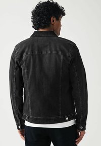 Schwarze Jeansjacke mit taillierter Passform, knöpfbarem Verschluss und zwei Seitentaschen. Sichtbare Nähte und eine strukturierte Oberfläche.