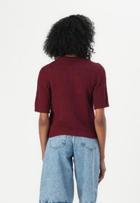 Maglione corto a maniche corte burgundy a lavorazione strutturata, abbinato a pantaloni corti in denim azzurro chiaro con tasche posteriori.