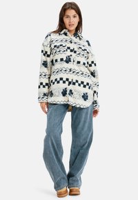 Fleece shirt in crème met marineblauwe geometrische en bloemmotieven. Voorzien van knoopsluiting, twee borstzakken en een ontspannen pasvorm. Gepaard met wijde jeans.