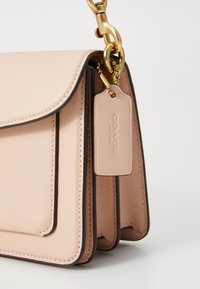 Light pink leather handbag with black trim, smooth texture, flap closure, and gold hardware. Features a tag embossed with "Coach."