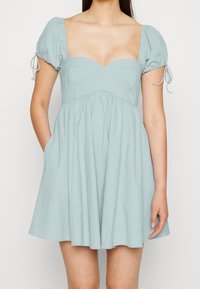 Ljusblå minikjol med en figurnära överdel, fyrkantig halsringning och puffärmar. Tillverkad av texturerad tyg med sidofickor för extra detalj.