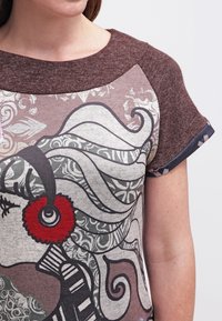 Parte superior marrón y gris con un diseño gráfico estampado con remolinos y acentos de hilo rojo en las mangas. Material de algodón suave con escote redondeado.