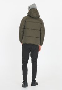 Olivengrøn pufferjakke med hætte, der har vandrette syninger, parret med sorte slim-fit bukser og sorte sneakers. Lys grå strikket hue.