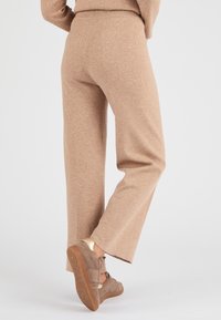 Pantaloni a maglia marrone chiaro con una vestibilità ampia, tessuto testurizzato e una cintura larga, abbinati a sneakers marroni con accenti dorati.