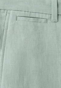 Tissu en lin vert clair montrant un gros plan d'un pantalon sur mesure avec une poche latérale et une boucle de ceinture à la taille.