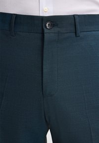 Close-up van donkerblauwe formele broek met een knoopsluiting en riemlussen, gedragen met een wit shirt.