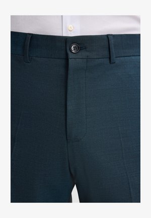 Close-up van donkerblauwe formele broek met een knoopsluiting en riemlussen, gedragen met een wit shirt.