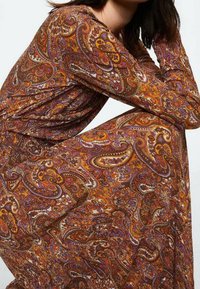 Pitkähihaisen, paisleykuvioisen mekon lämpimät ruskea, oranssi ja violetti sävyt. Slim fit -leikkaus, pehmeä tekstuuri, jossa on monimutkaisia pyörteitä ja kuvioita.