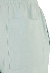Light mint green fabric with a ribbed texture, featuring a square pocket and elastic waistband. Simple design with visible stitching details.