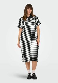 Černobílé pruhované krátké šaty s krátkým rukávem, vybavené polokošilovým límečkem a bočními rozparky pro snadný pohyb. Nošeny s černými botami a bílými ponožkami.