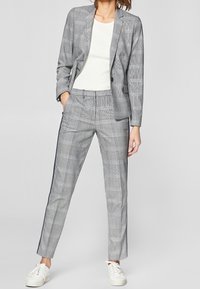 Grijs geruit pak met een getailleerde blazer en op maat gemaakte broek. Gladde stof met een subtiele glans, gecombineerd met witte sneakers.