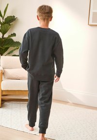 Black sweatshirt and matching pants made of soft fabric, featuring ribbed cuffs and a relaxed fit. Minimalist design, with no visible patterns.