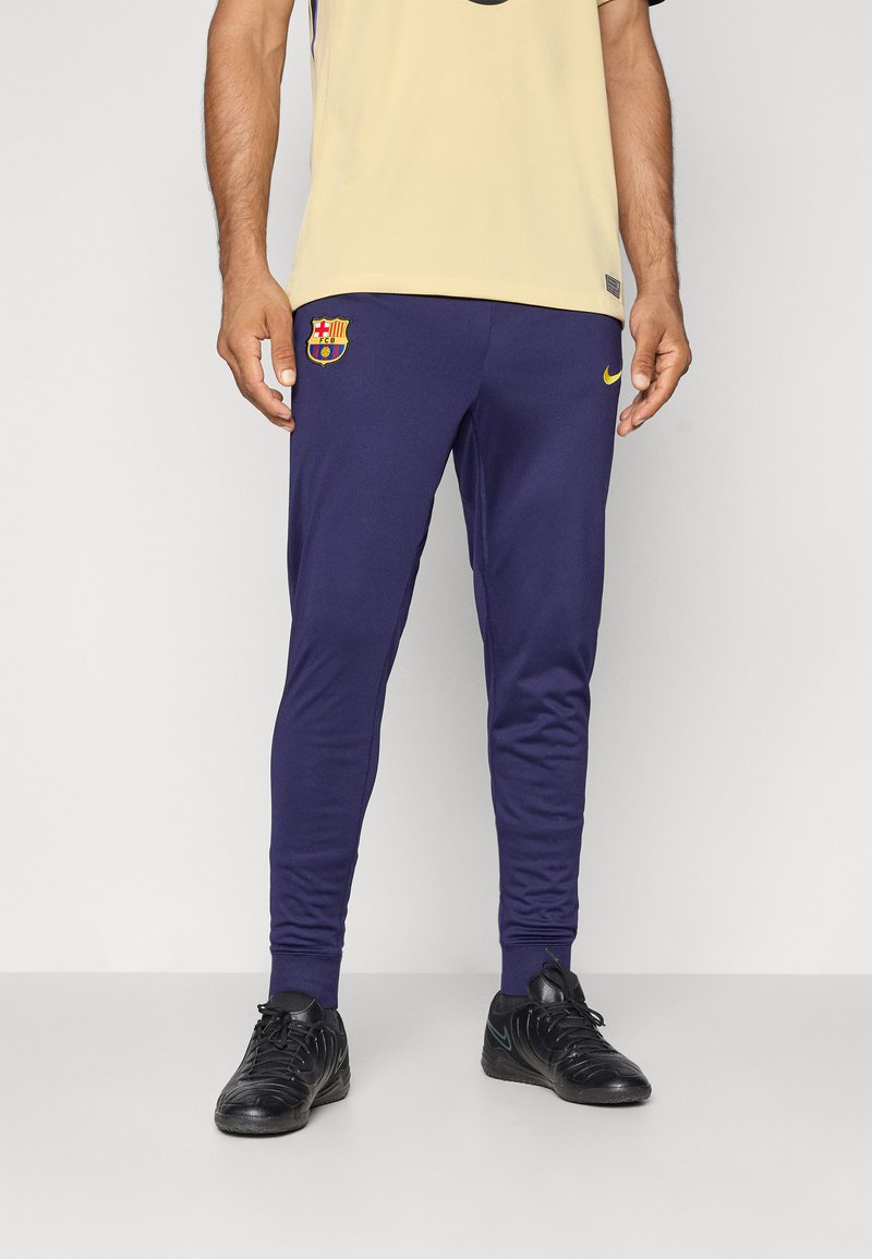 Marineblauwe sportbroek met een slim fit, voorzien van een Barcelona-logo en een gele Nike-swoosh. Gemaakt van een glad, rekbaar materiaal voor extra comfort.