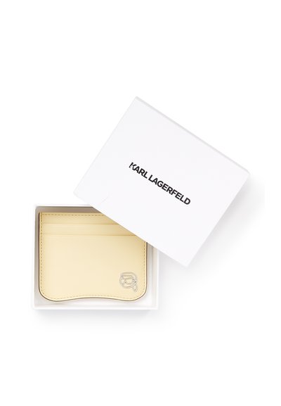 Porte-cartes en cuir crème avec logo Karl Lagerfeld dans une boîte blanche avec texte de la marque noir sur le couvercle, légèrement ouvert.