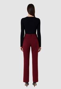 Pantaloni su misura bordeaux con vestibilità dritta, vita media, tasche posteriori e scarpe nere con tacco alto.