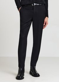 Pantaloni neri su misura in tessuto strutturato, con taglio aderente e leggermente affusolati, abbinati a stivaletti neri e cintura nera.