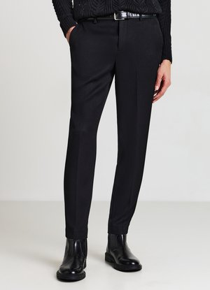 Schwarze maßgeschneiderte Hose aus strukturiertem Stoff mit schmaler Passform und leicht zulaufendem Bein, kombiniert mit schwarzen Stiefeletten und einem schwarzen Gürtel.