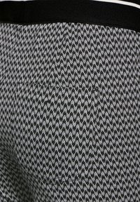 Black and white houndstooth patterned fabric with a visible stitched pocket and black waistband with white stripes.