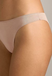 Világos rózsaszín tanga alsónemű sima anyagból, vékony derékszíjjal és minimalista dizájnnal, finom varrási részletekkel.