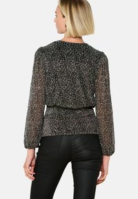 Top nero trasparente con motivo leopardato, maniche lunghe a palloncino e vita arricciata. Abbinato a pantaloni neri attillati.