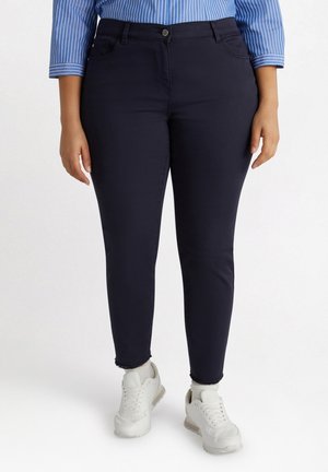 Diepblauwe skinny jeans in een gladde stof met een lichte glans, voorzien van een voorste knoopsluiting en vijf zakken. Ongelijke zoomdetails.