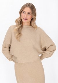 Beige gebreide trui met ribbels, hoge halslijn, verlaagde schouders en lange mouwen, ontworpen voor een losse, comfortabele pasvorm.