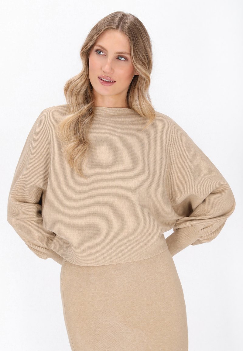 Beige gebreide trui met ribbels, hoge halslijn, verlaagde schouders en lange mouwen, ontworpen voor een losse, comfortabele pasvorm.