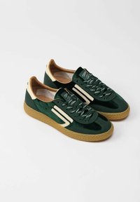 Sneaker in suede verde con suola in tann beige texturizzata, strisce crema e lacci a motivo. Caratterizzati da una forma arrotondata e un interno imbottito.