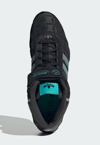 Čierne vypchávkové tenisky s textúrovaným zvrškom, tromi tyrkysovými pruhmi, kontrastnou tyrkysovou vnútornou podšívkou a plochým šnurovaním.