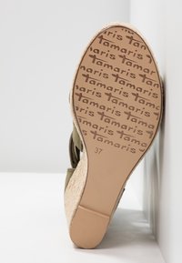 Sandale compensée avec une semelle en jute tressé texturée, tige vert olive et une semelle intérieure lisse ornée de lettres de la marque répétées et de la taille 37.